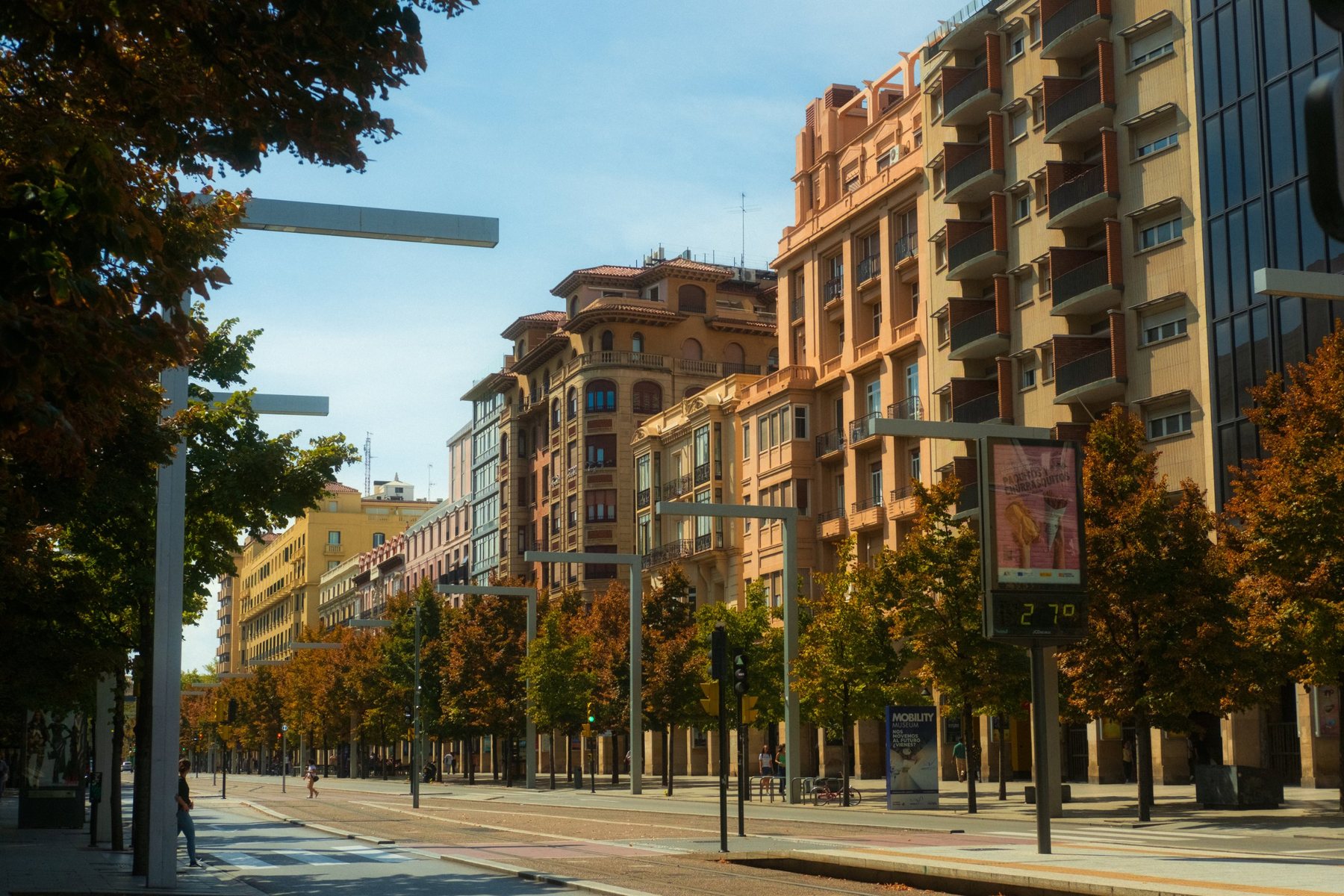 A wide city avenue lined with autumn trees and warm apartment buildings in afternoon sun