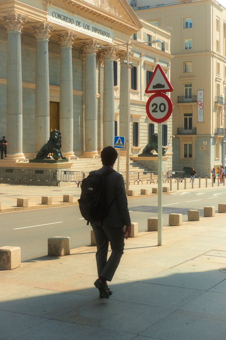 A man in a suit walking past the columns and stone lions of the Congreso de los Diputados