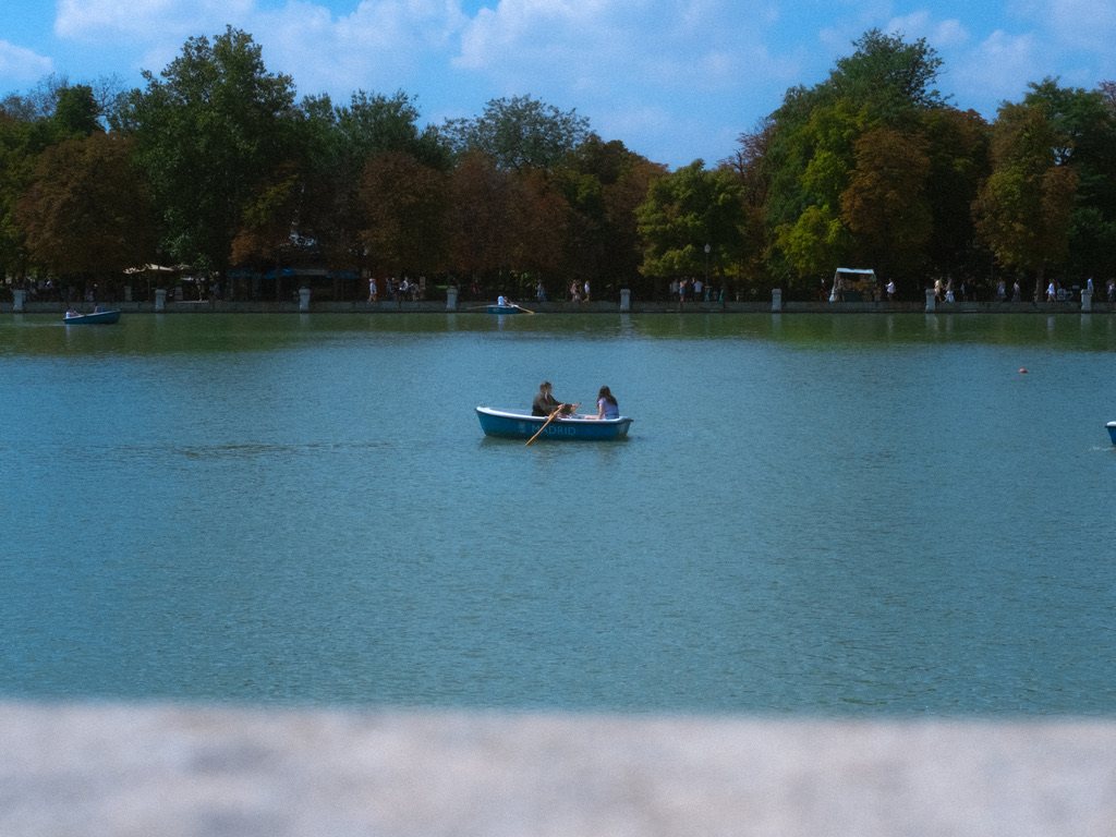 Two people in a small blue rowboat on a green lake with trees behind