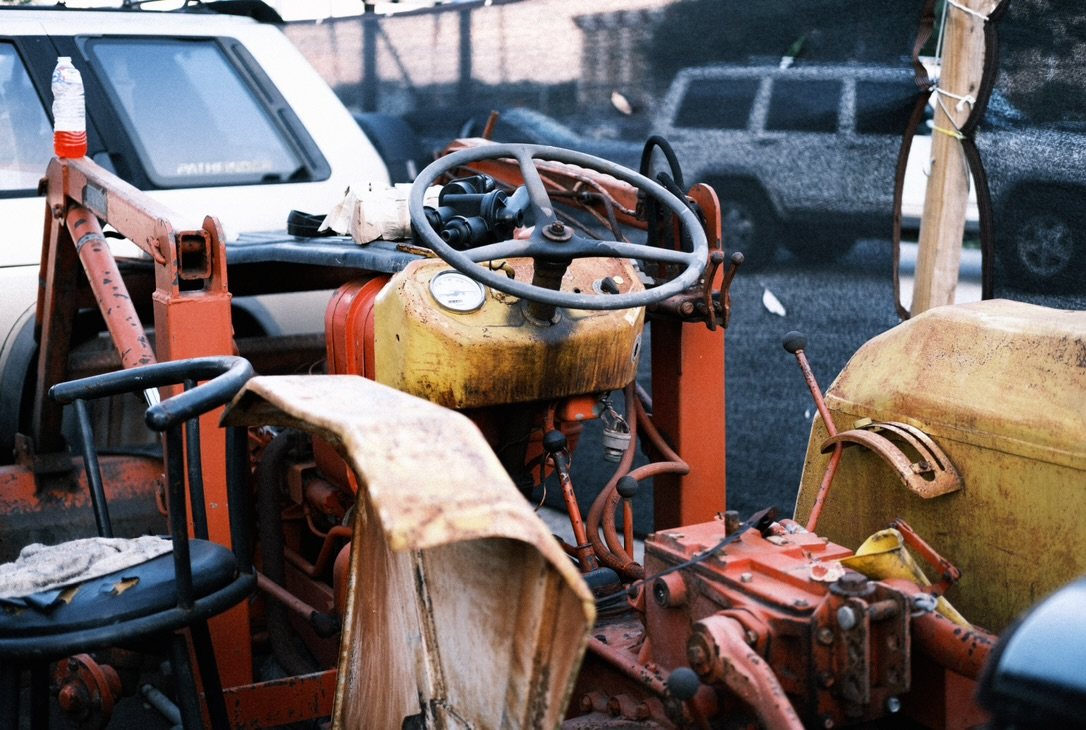 A weathered yellow and orange tractor parked in a lot with its steering wheel and gauge visible
